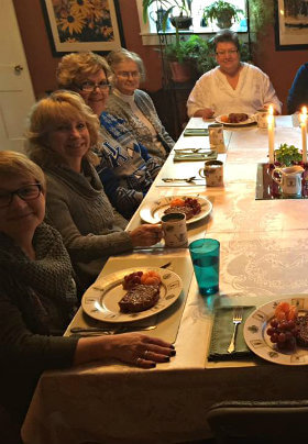 Group of ladies at a table with a white tablecloth, candles and green centerpiece.