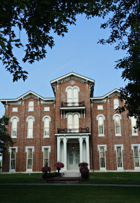 Tall brown historic building with four tall pillars in front and several tall windows.