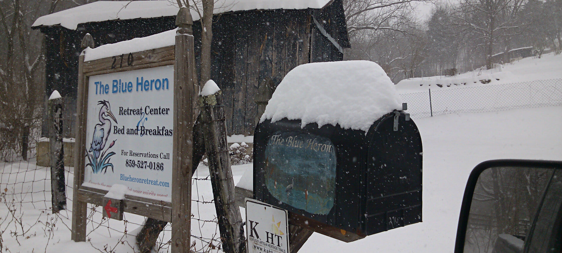 A large framed white sign with Blue Heron logo and painted mailbox welcome guests to the farm.