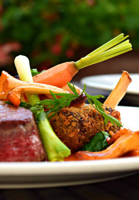 A delicious plate of grilled steak with fresh yellow carrots and seasonal vegetables.