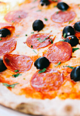 A hot and delicious pizza with red pepperoni and black olives and seasonings.